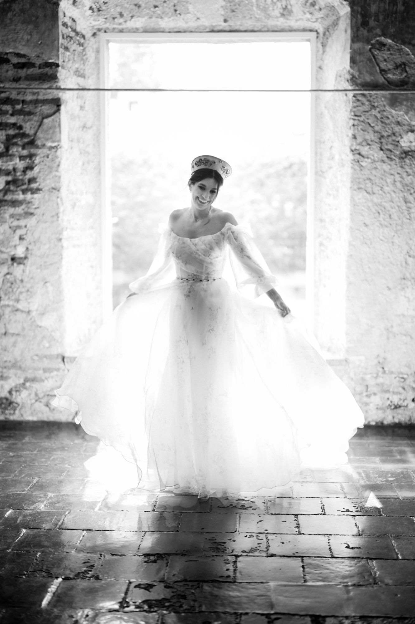 Backlit bridal silhouette in a stone window frame creating an ethereal glow effect.
