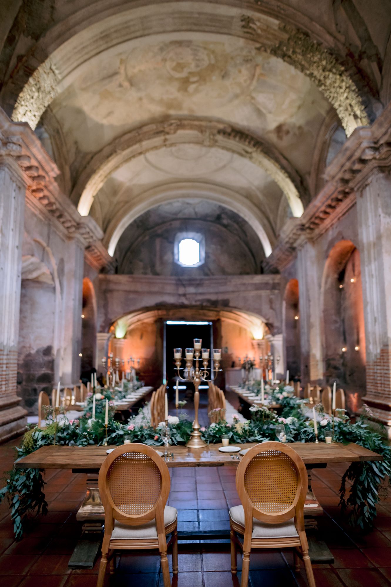 Cathedral venue with vaulted ceilings and long banquet table decorated with candlelight and greenery.