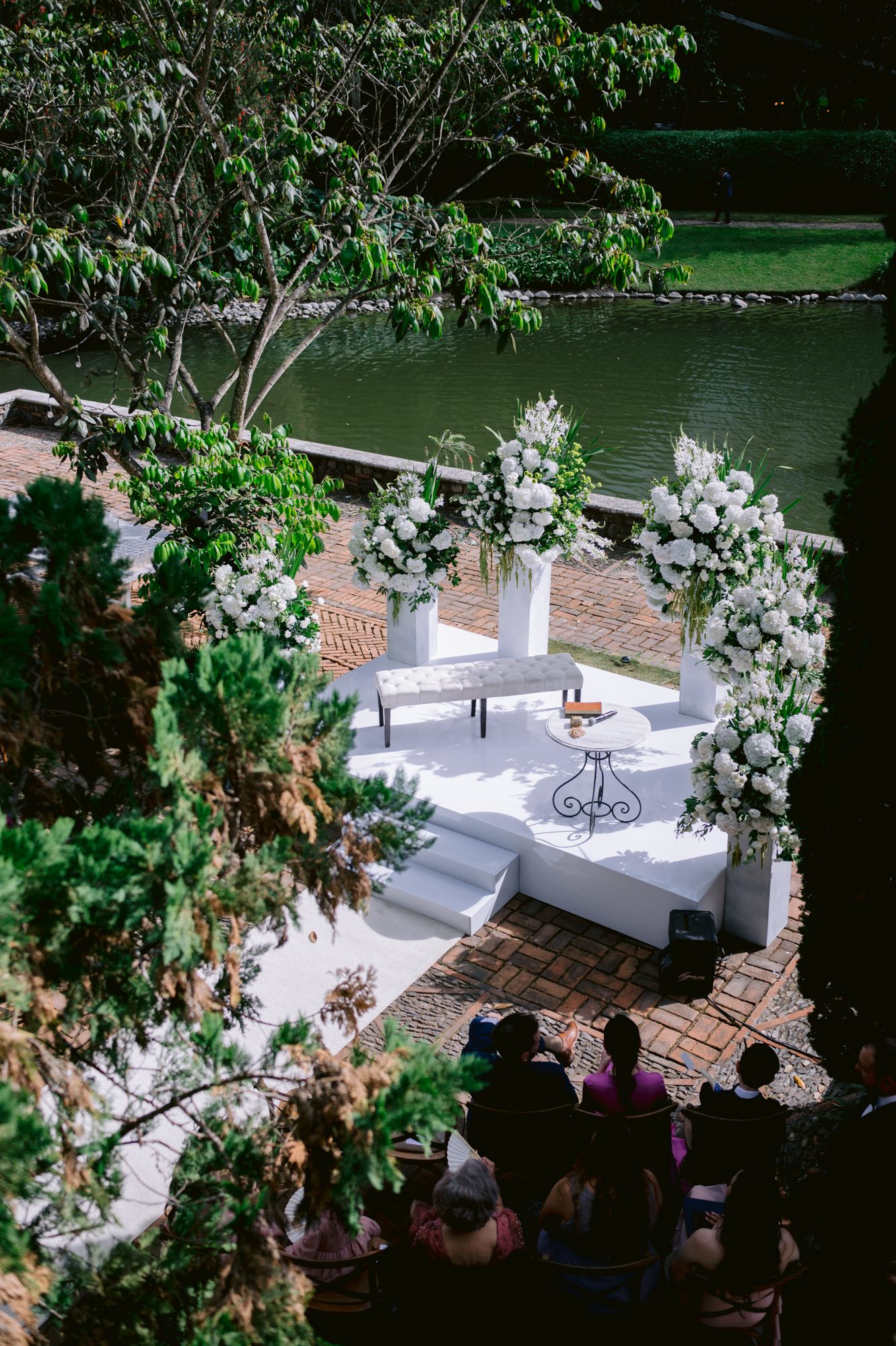 Elegant outdoor wedding ceremony setup with white floral arrangements and seating by a serene lake.