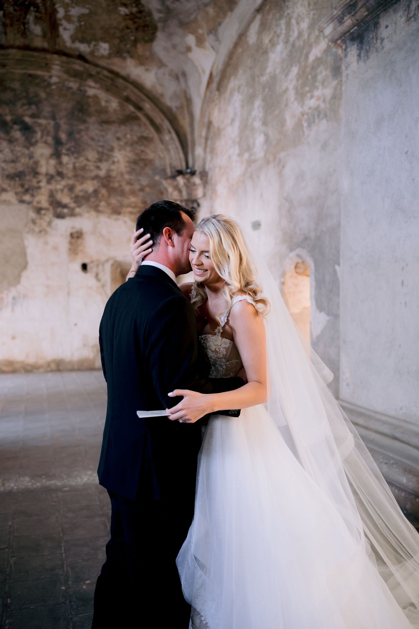 Intimate wedding portrait shows couple sharing romantic moment in stone hallway.
