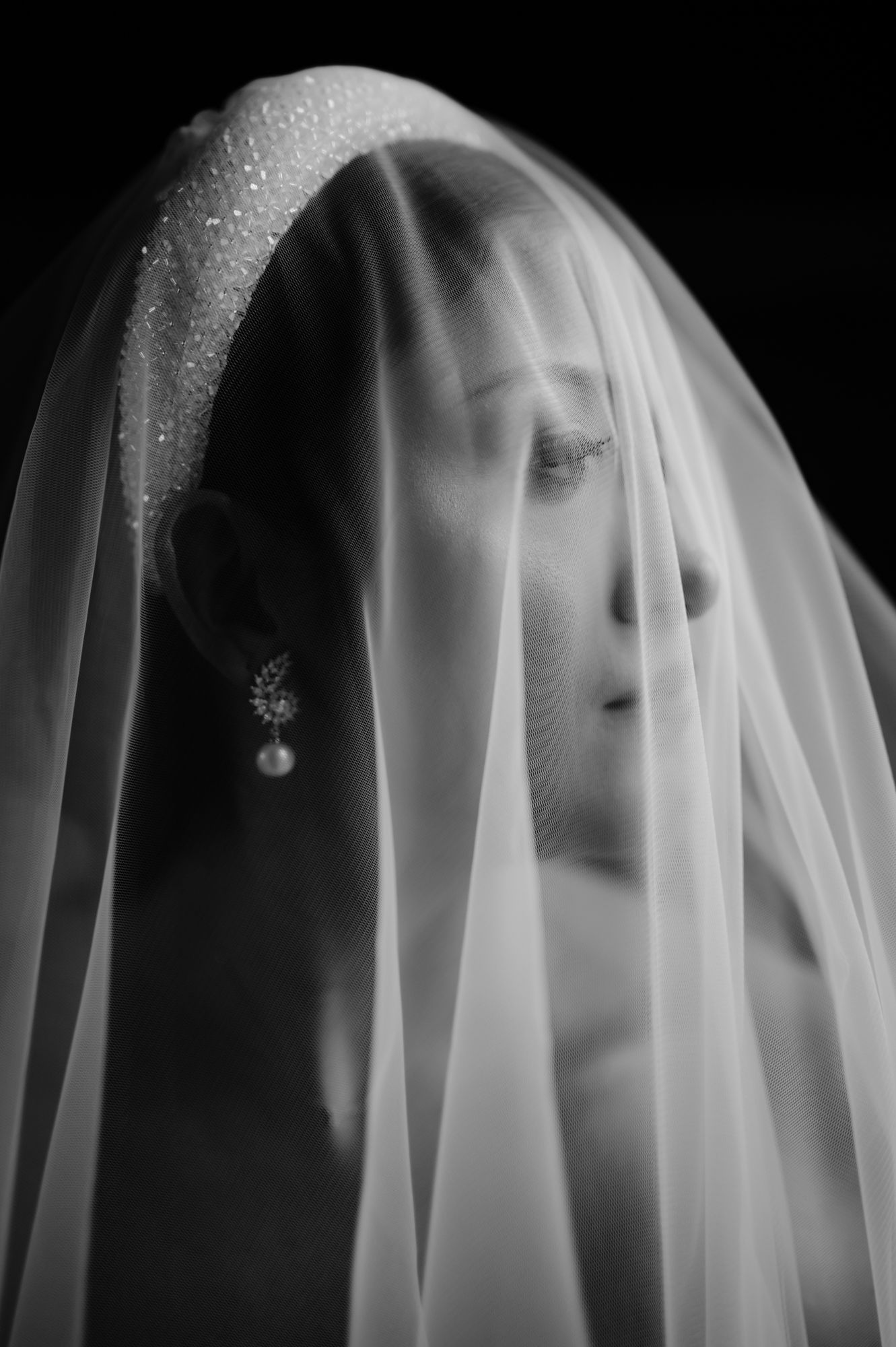 Ethereal black and white portrait of bride with delicate veil creating soft, dreamy effect.