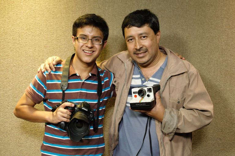 Two photographers smile while holding vintage cameras.