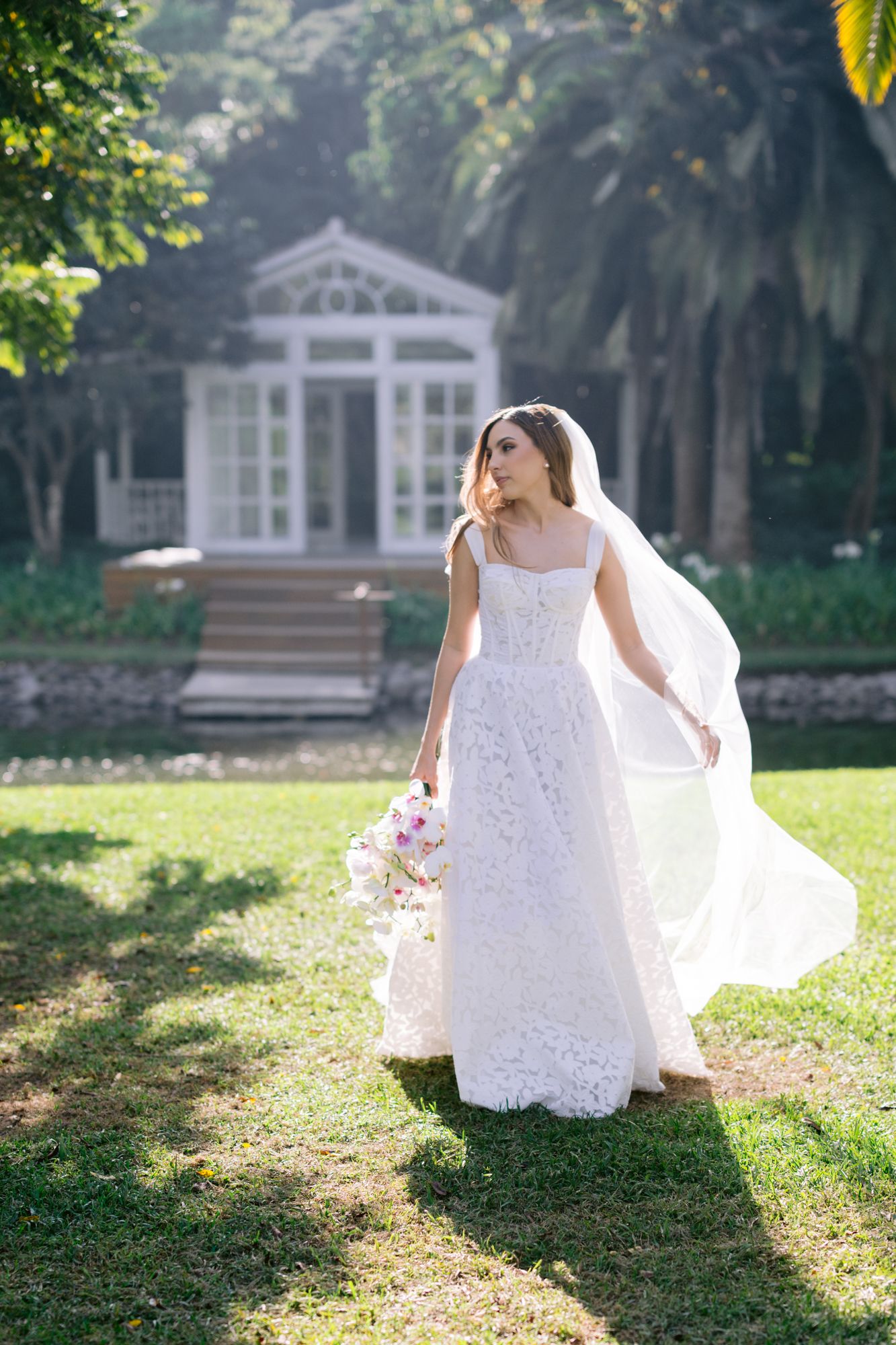 A flowing white wedding dress catches sunlight in a garden with white gazebos in the background.