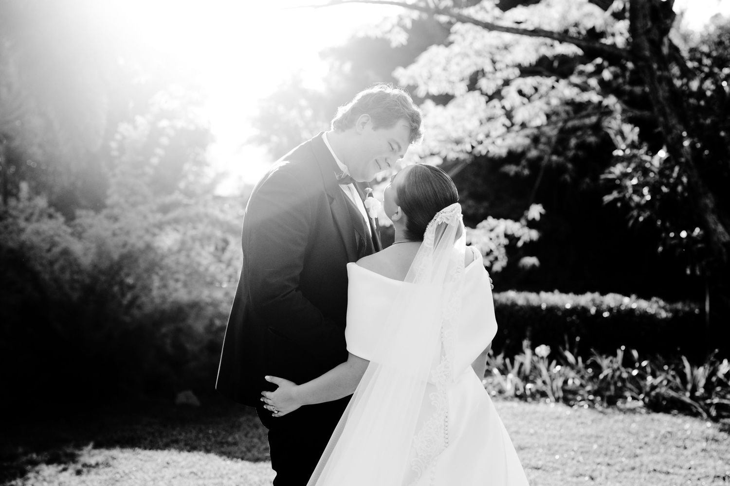 Black and white silhouette of a romantic wedding moment in a sunlit garden setting.