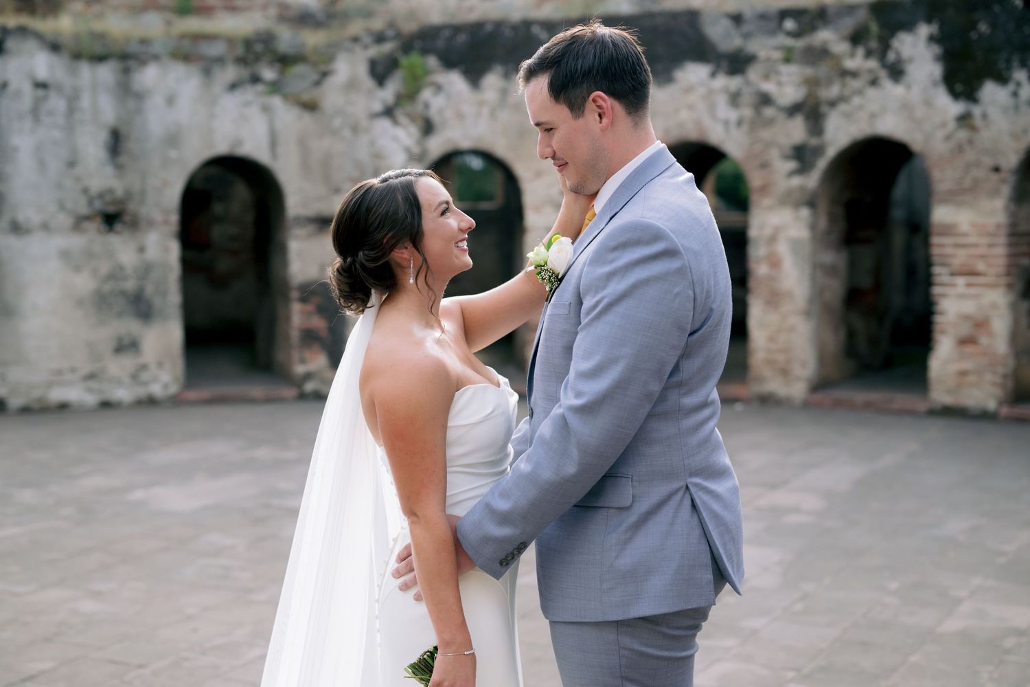 Romantic wedding portrait of couple embracing in front of weathered stone archways.