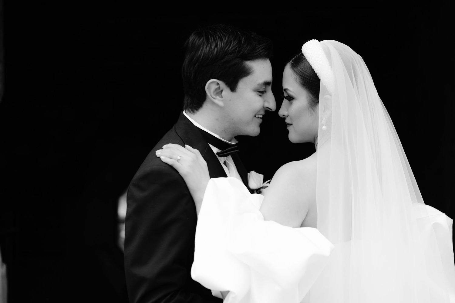 An intimate black and white wedding portrait captured against a dark background.