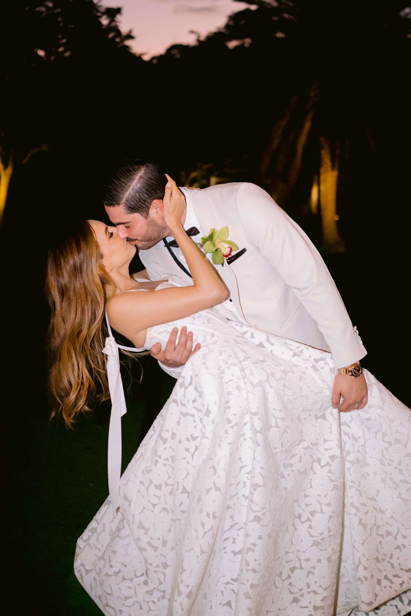 A romantic dip kiss between newlyweds at sunset, with the bride wearing an elegant white lace wedding gown.