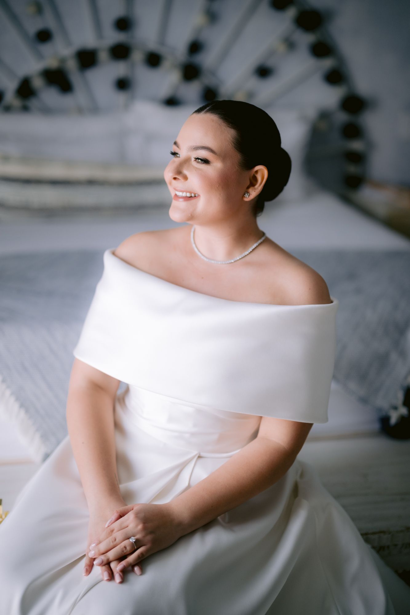 Elegant off-shoulder white wedding dress with folded neckline detail shown against a decorative headboard.