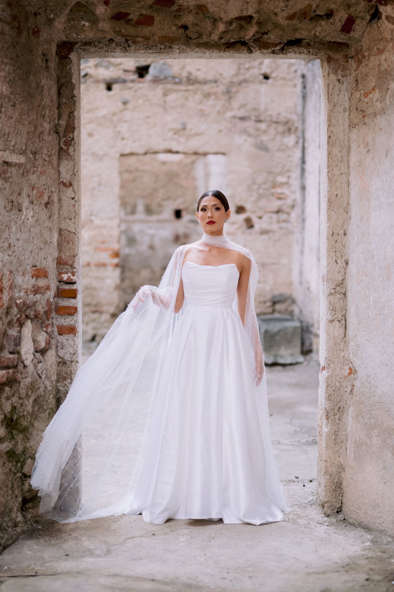 Stunning bridal gown with strapless design and billowing skirt posed in historic stone archway.