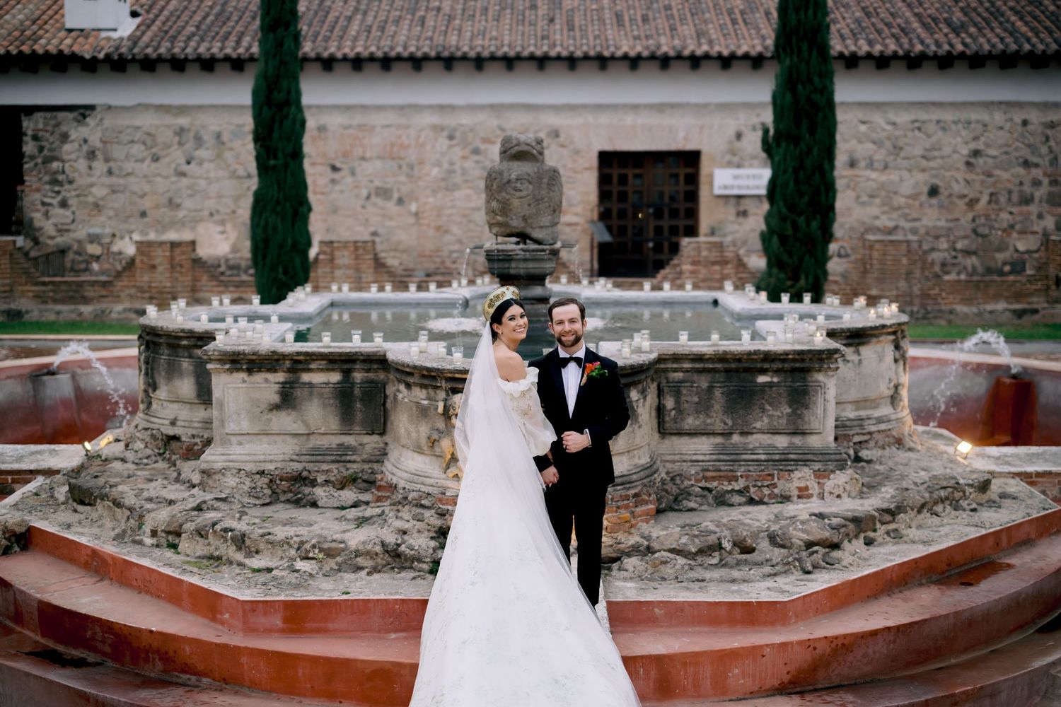 Newlyweds pose together on stone steps of a historic mission-style building.