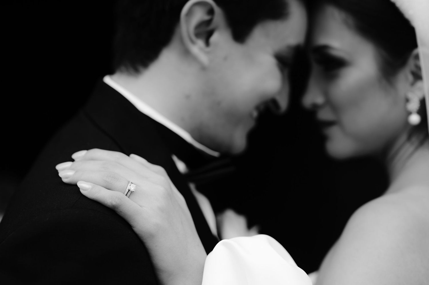 An intimate black and white wedding portrait showing clasped hands and tender moment.