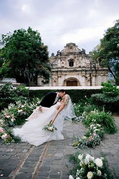 A romantic wedding scene with floral decor in front of an ornate Spanish colonial church facade in Antigua, Guatemala.