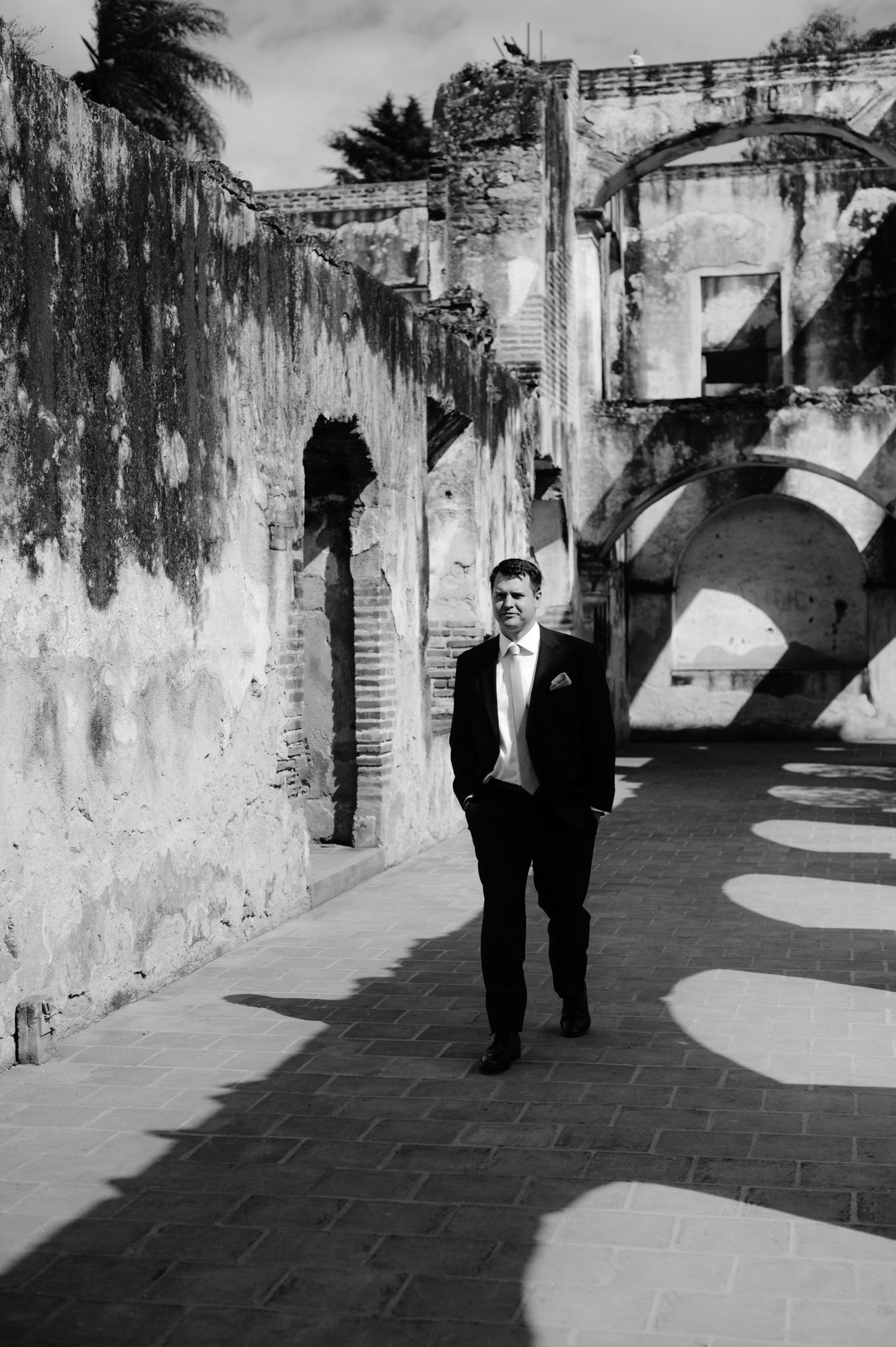 Black and white photo of a groom walking along an architecturally striking pathway.