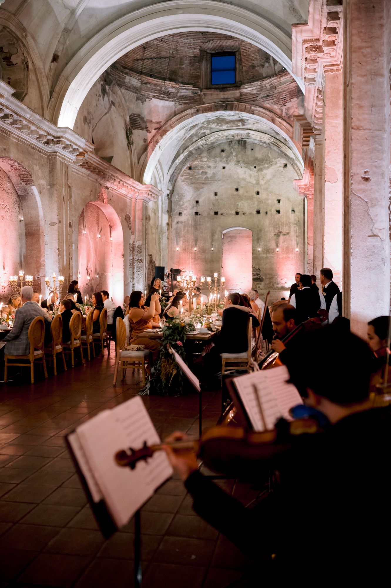 Musicians perform at wedding reception in historic venue with arched ceilings and ambient lighting.