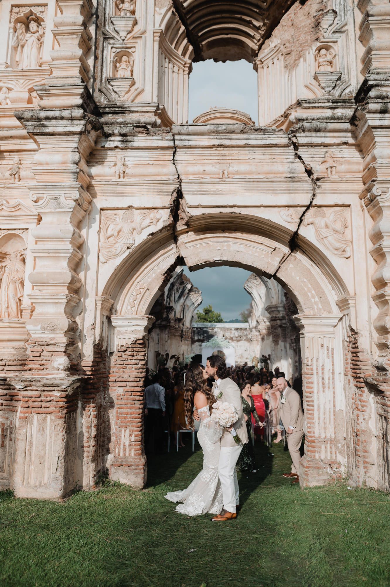 Wedding couple poses beneath historic stone arches in a romantic garden setting during their celebration.