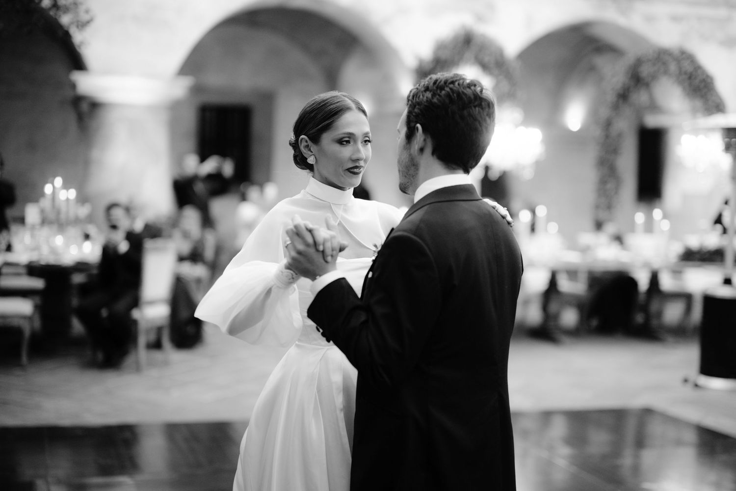 Romantic first dance in a historic arched venue with soft lighting.