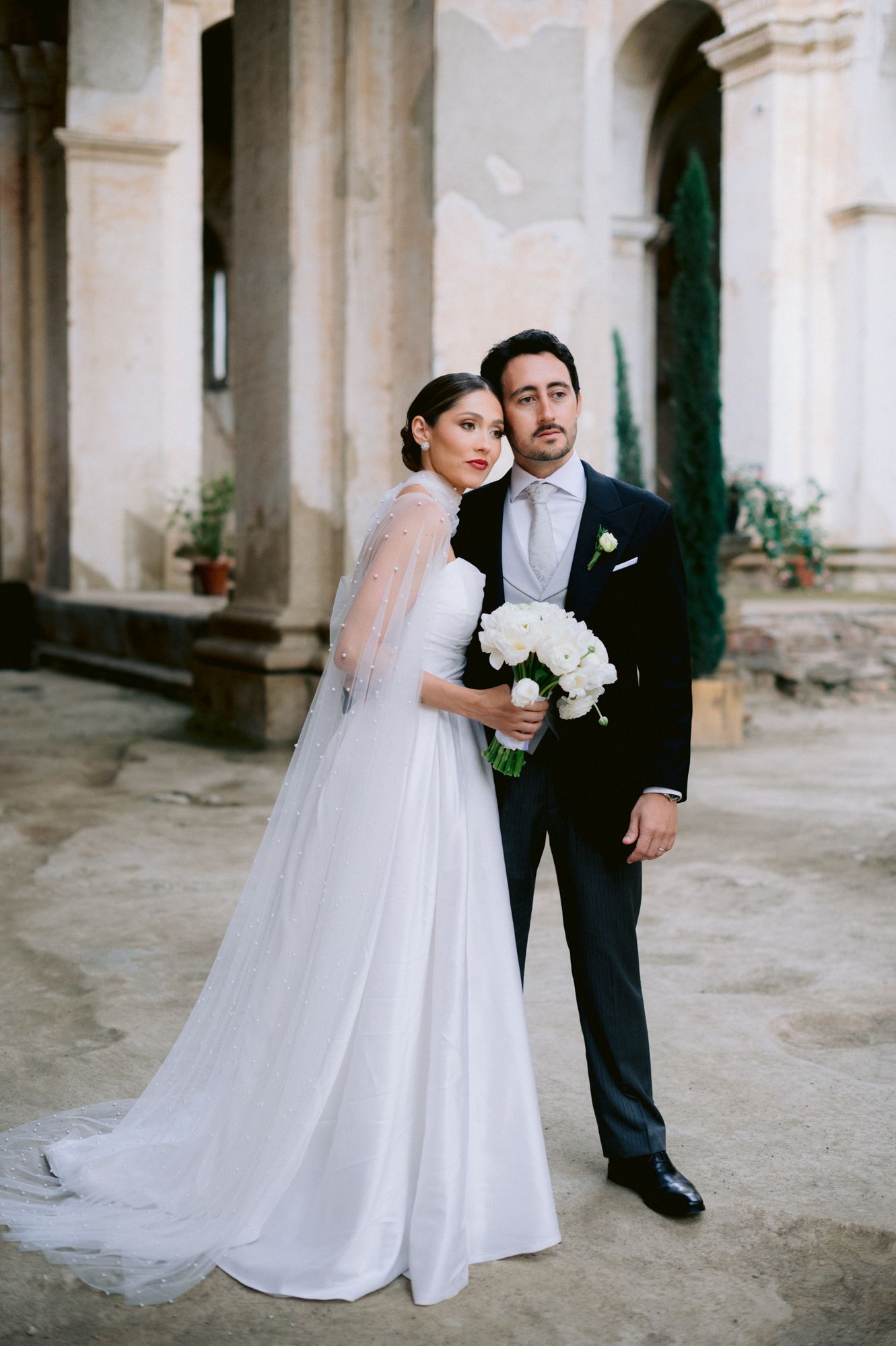Elegant wedding portrait of couple in formal attire posing against historic stone architecture.