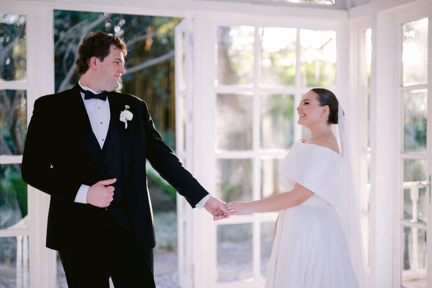 Newlyweds share a playful moment in a sunlit white conservatory during their wedding photoshoot.