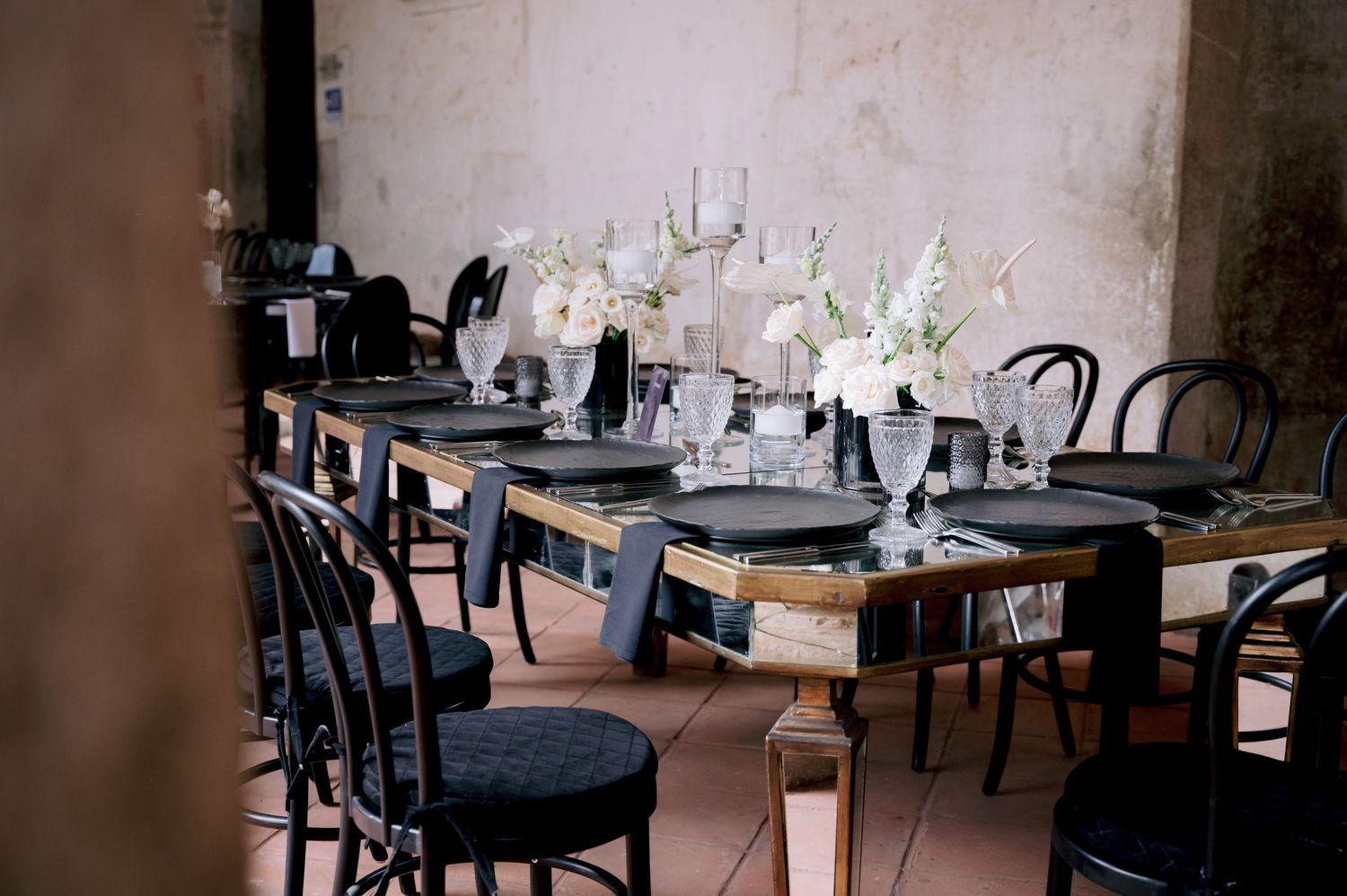 Elegant wedding table setting with black chairs and white floral centerpieces in rustic venue.