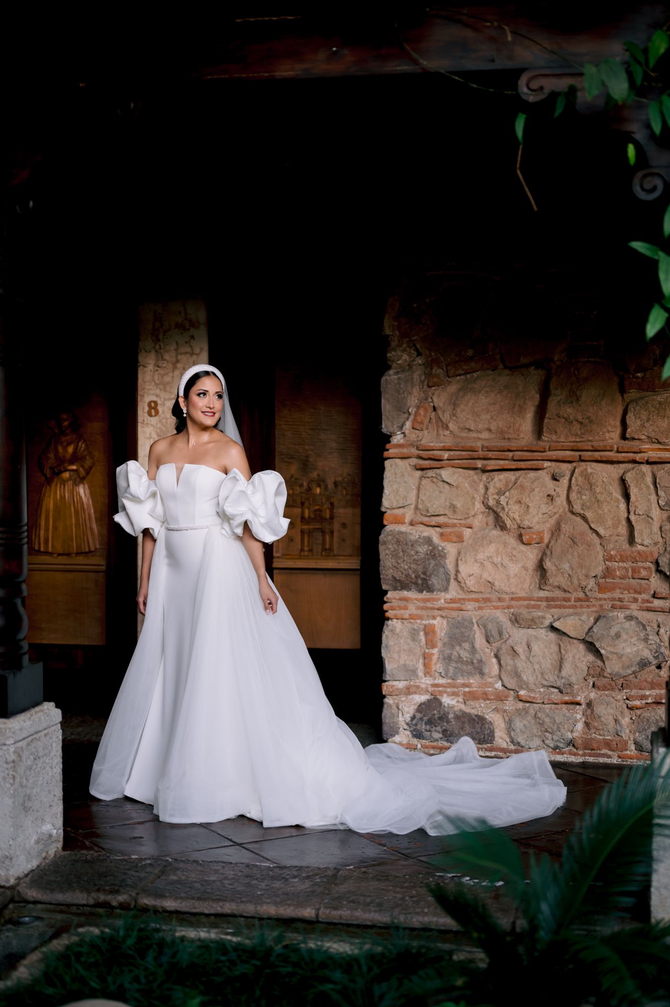 Bride wearing a classic white wedding dress with statement sleeves stands in a rustic stone corridor.