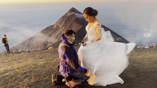 A proposal moment captured at sunset on a mountain peak above the clouds.