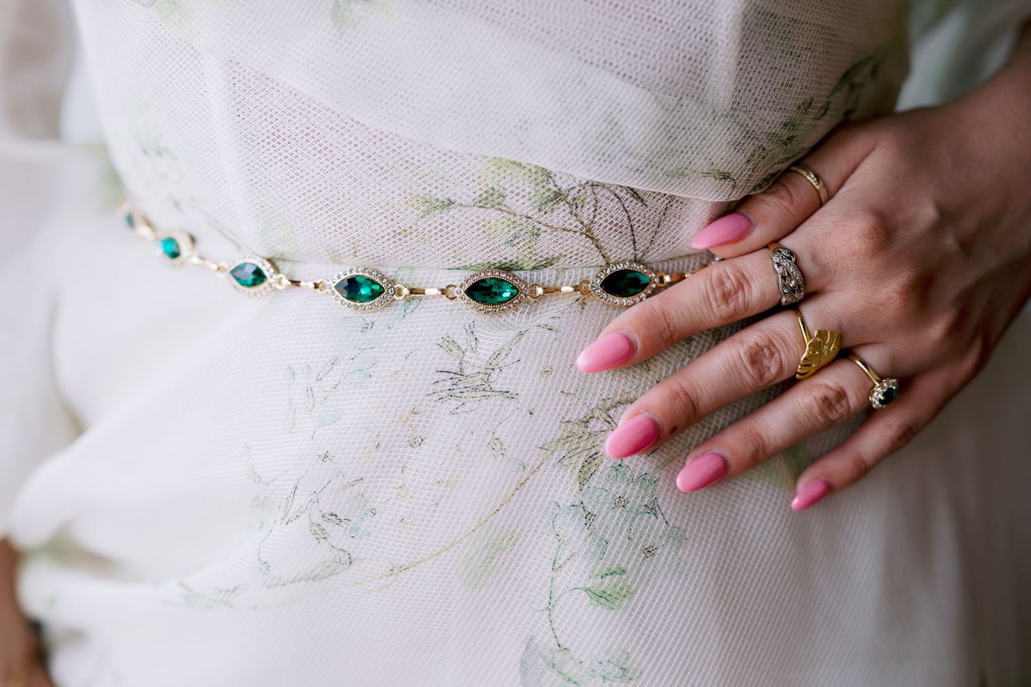 Close-up of bridal accessories showing emerald and crystal belt detail with rings.