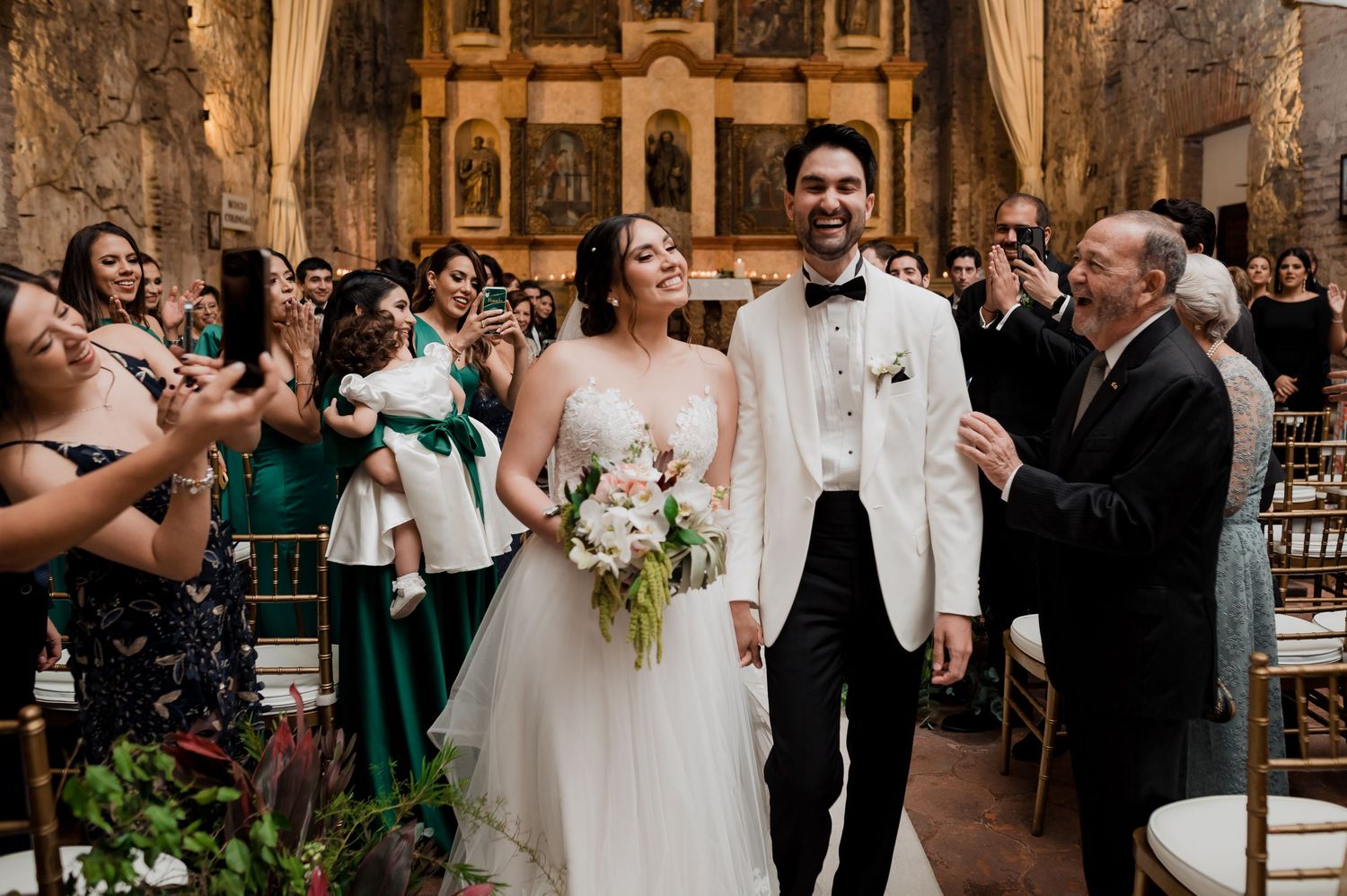 Wedding guests celebrate with newlyweds during recessional in historic church setting.