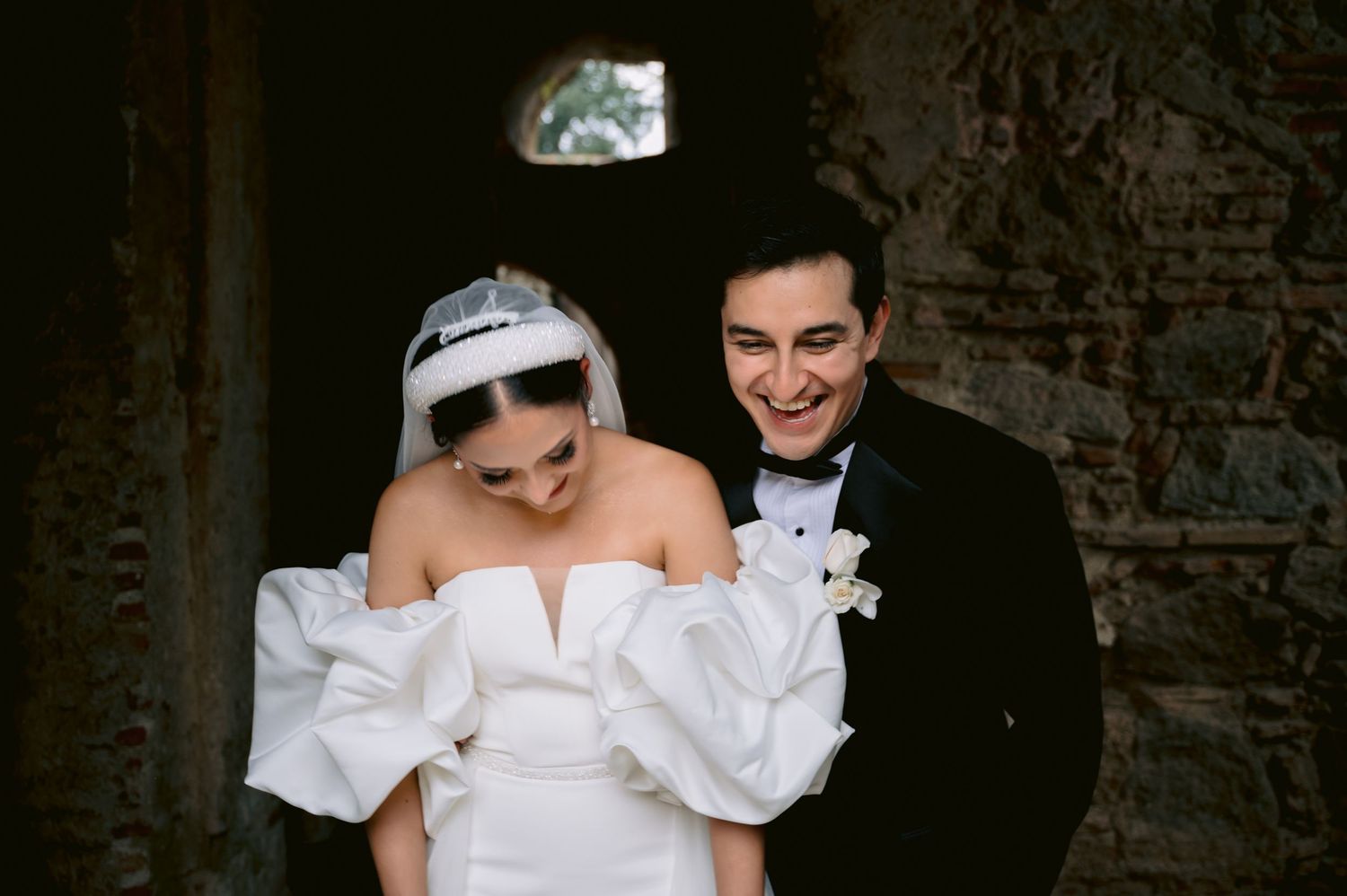 Candid moment of newlyweds sharing laughter in rustic stone setting.