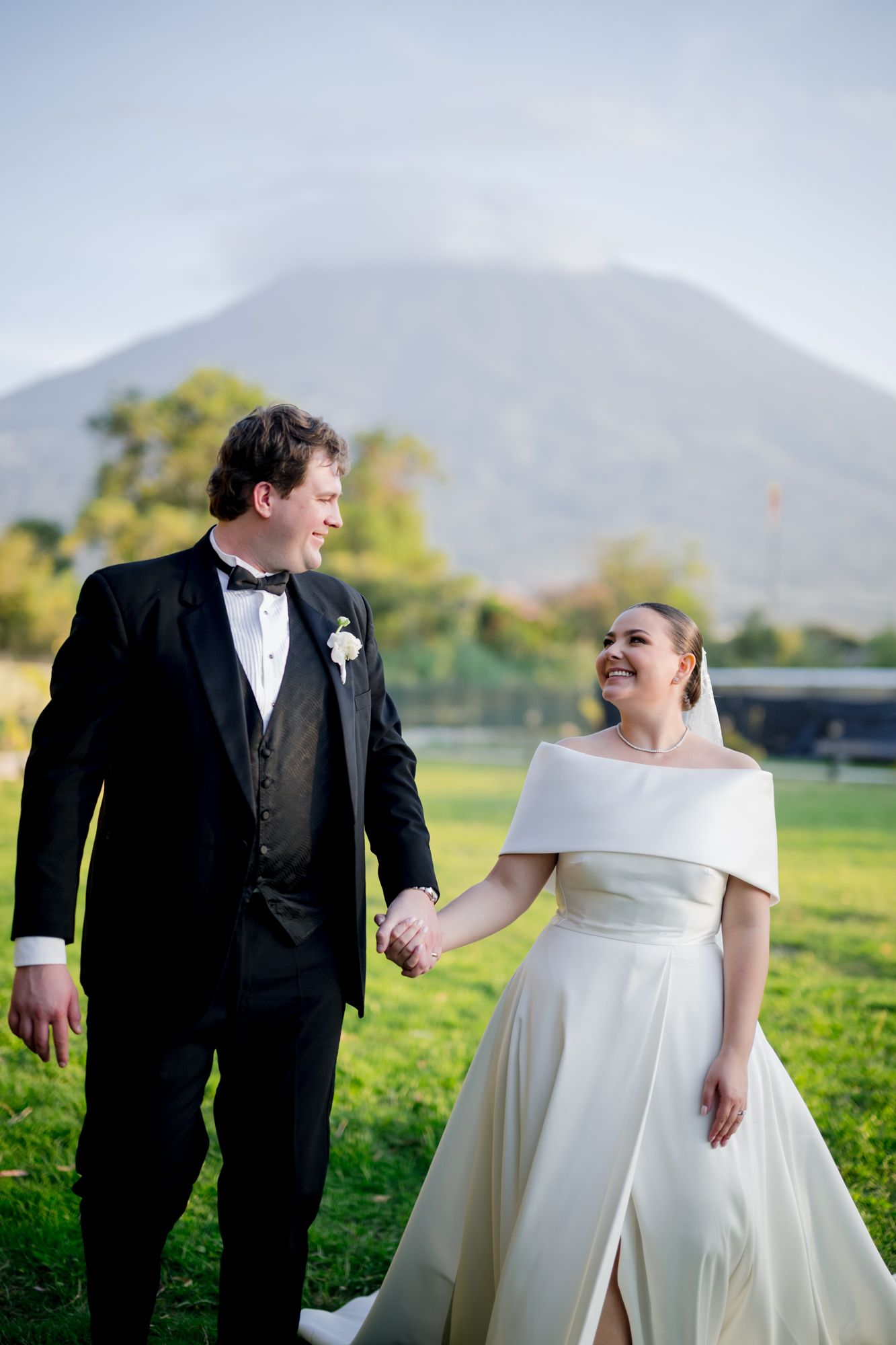 Wedding couple sharing joyful moment against mountain backdrop in formal attire.