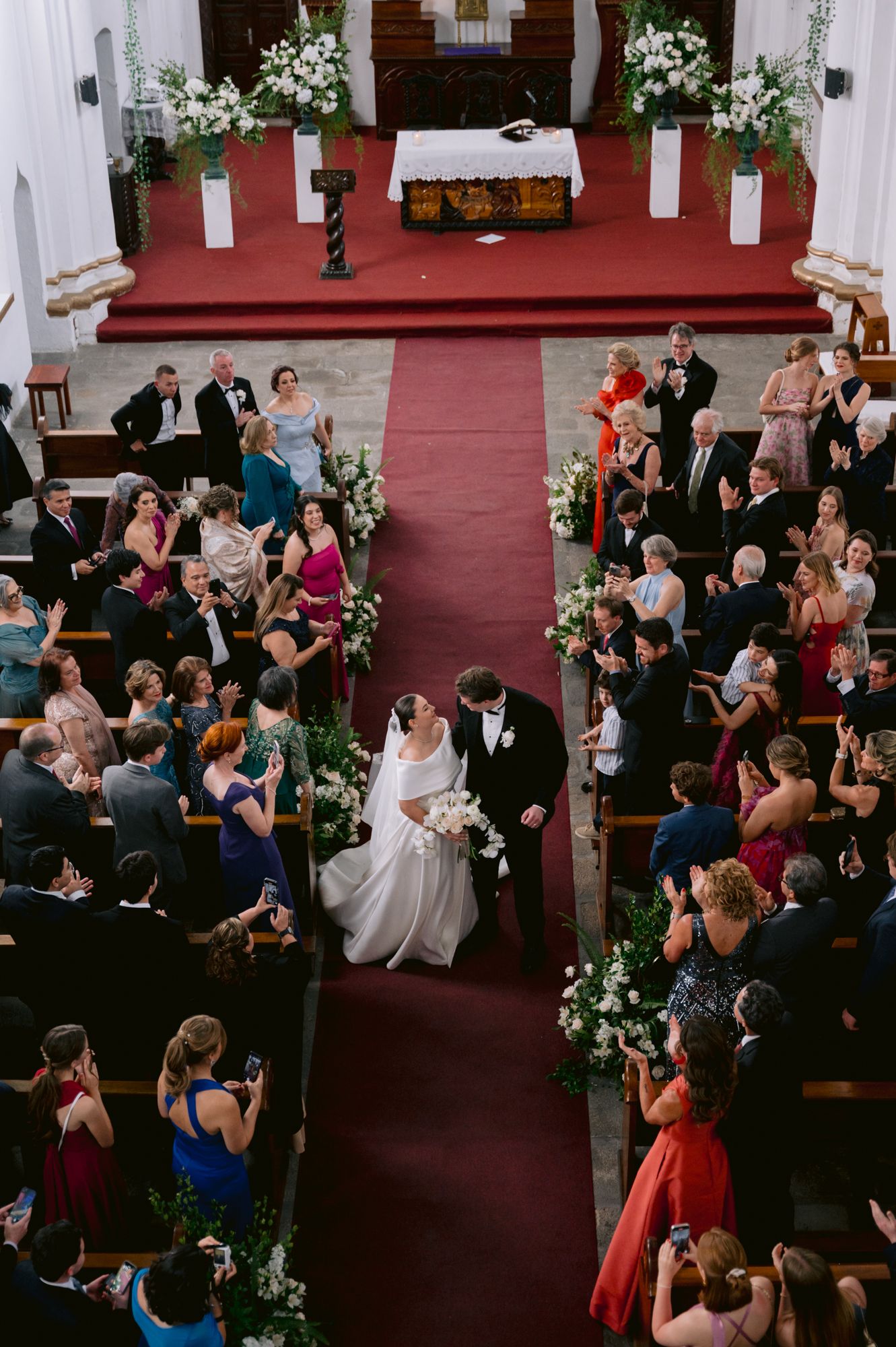 Overhead view of a church wedding ceremony with guests capturing photos of the happy couple.
