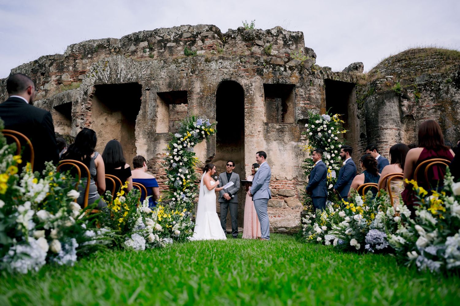 Intimate wedding ceremony set among ancient stone ruins with floral archways.