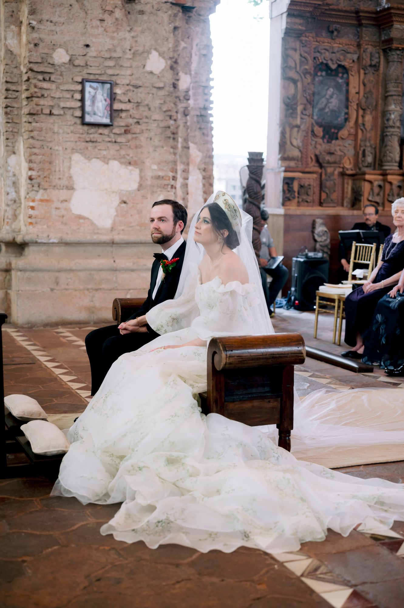 A couple seated at the altar during their wedding ceremony in a historic church with exposed brick walls.
