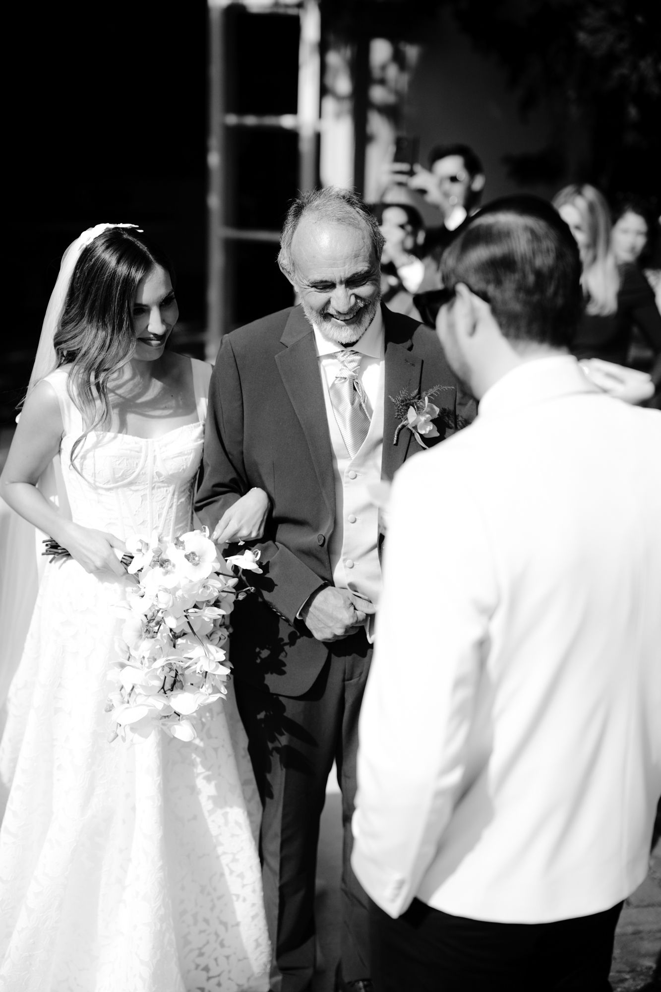 Black and white photo of a traditional wedding ceremony processional with a bride in white lace gown and bouquet.