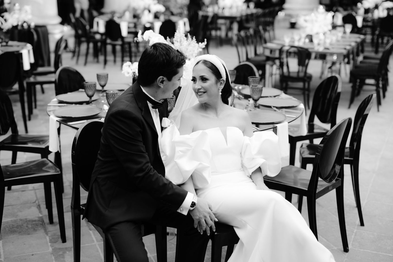 Intimate black and white portrait of newlyweds sitting in elegant reception chairs.