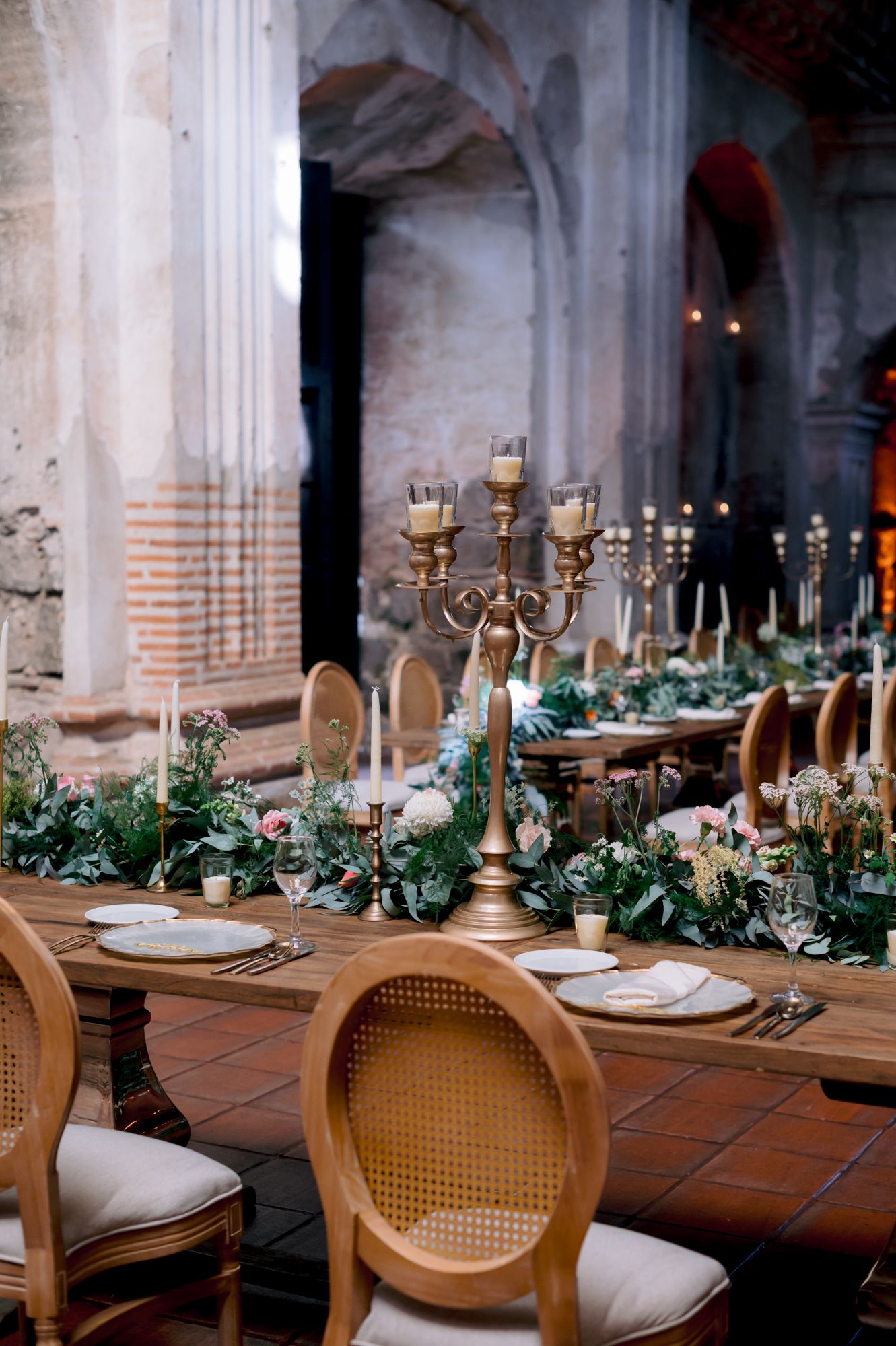 Elegant wedding reception table with gold candelabras and greenery in a historic church setting.