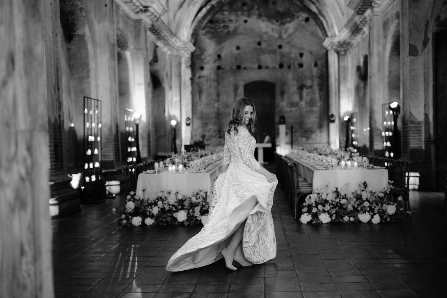 Black and white photo of bride spinning in decorated historic venue with arched ceilings.