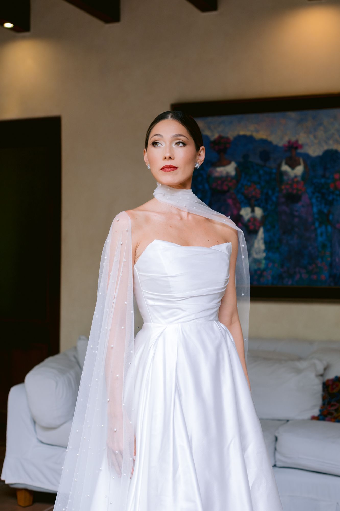 A stunning white wedding gown with strapless neckline and flowing cape detail.