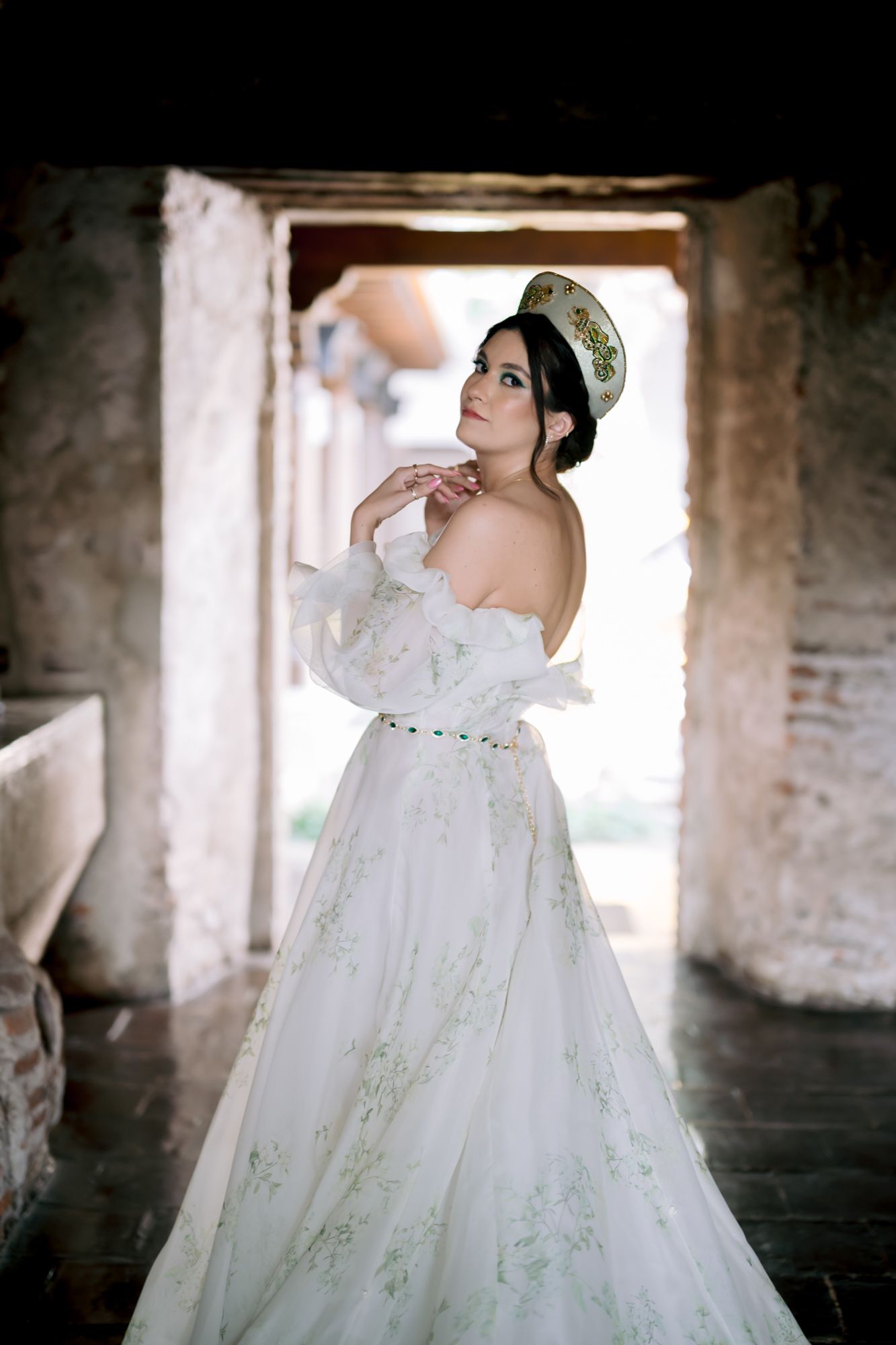 Ethereal bridal portrait in a white gown with delicate embroidery standing in a rustic stone archway.