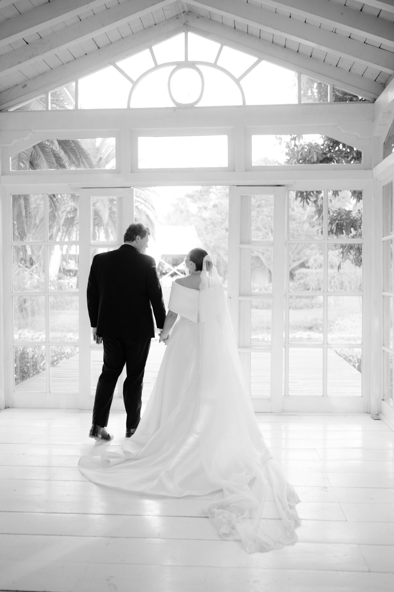 Black and white wedding portrait showing couple against architectural windows in bright conservatory.