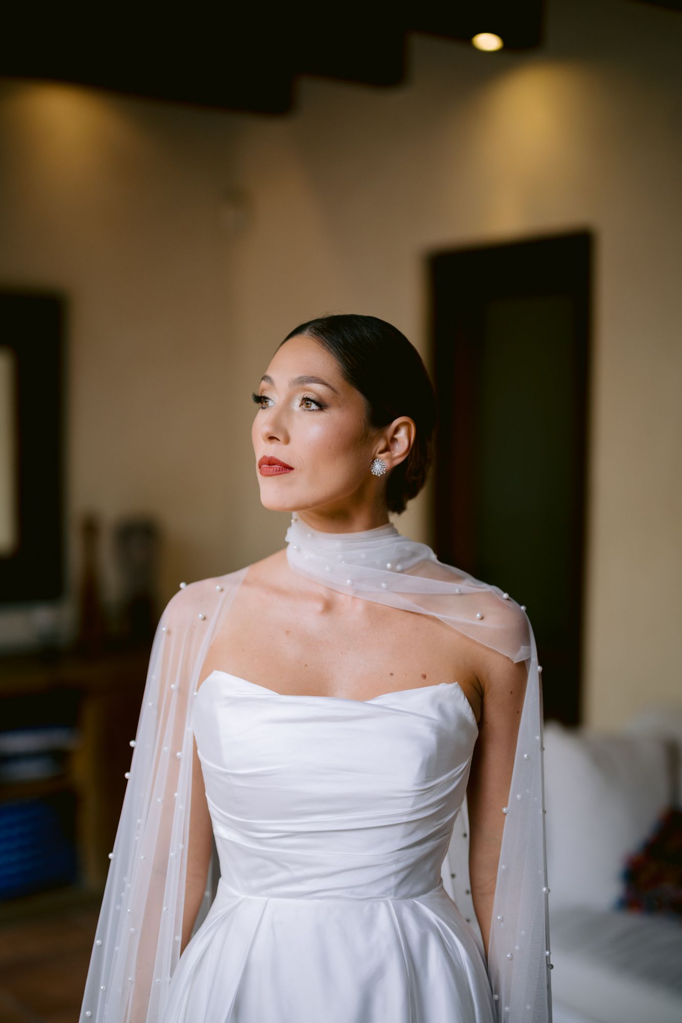 Elegant bride wearing a strapless white wedding gown with pearl-adorned sheer cape.