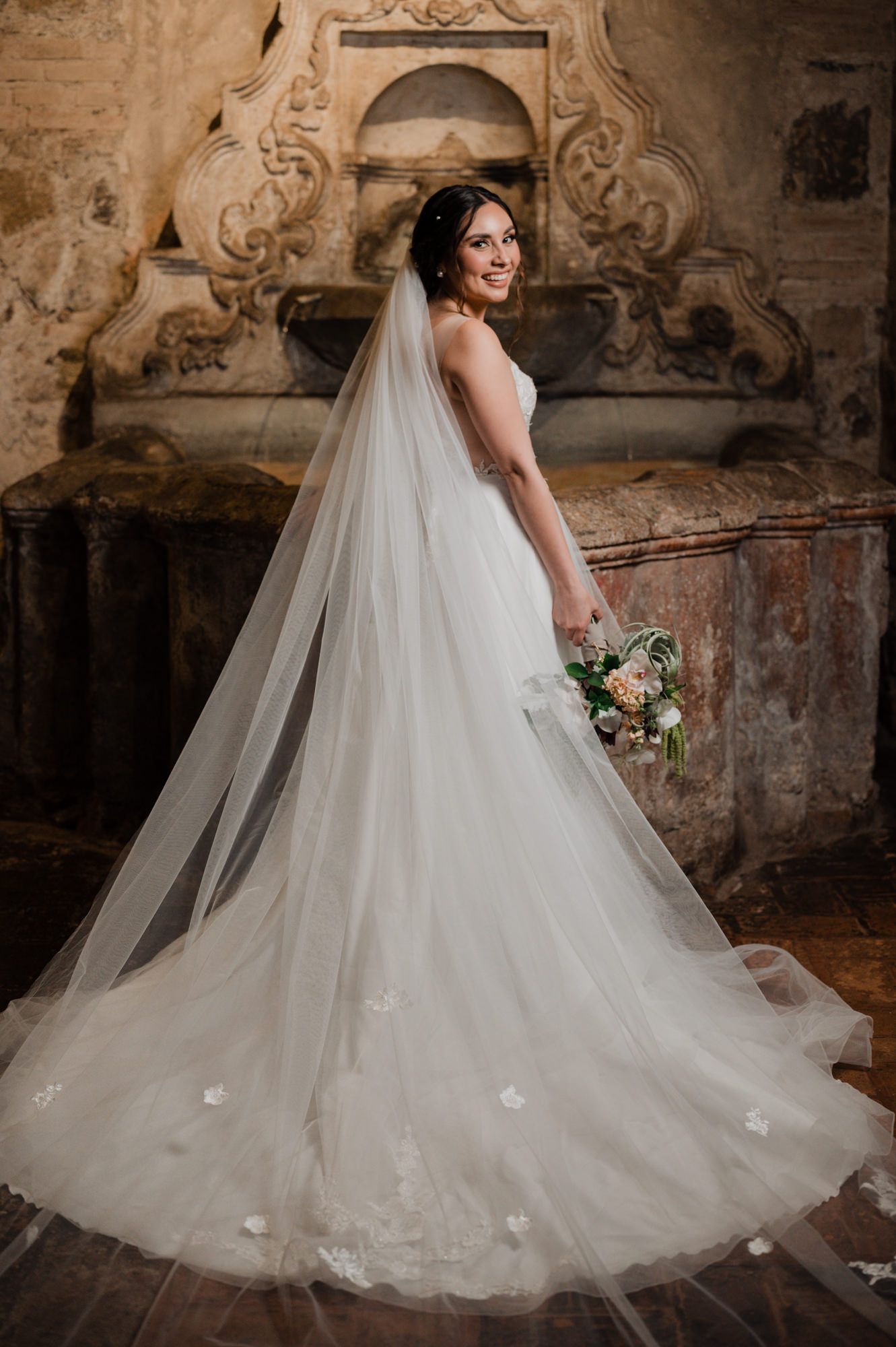 Bridal portrait showcasing flowing veil and train against vintage stone backdrop.
