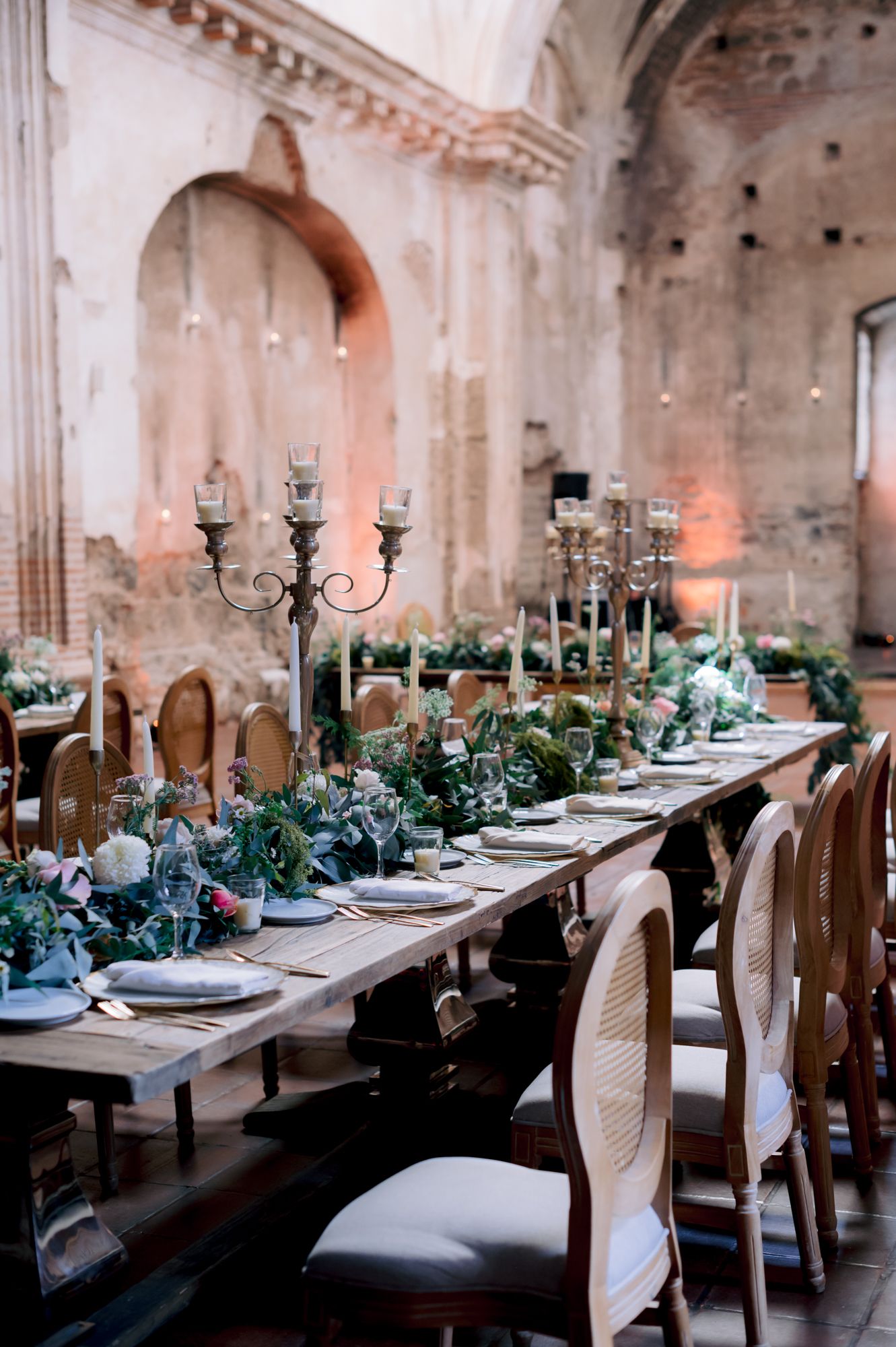 Elegant table setting in historic church with ornate candelabras and greenery garlands in rustic venue.