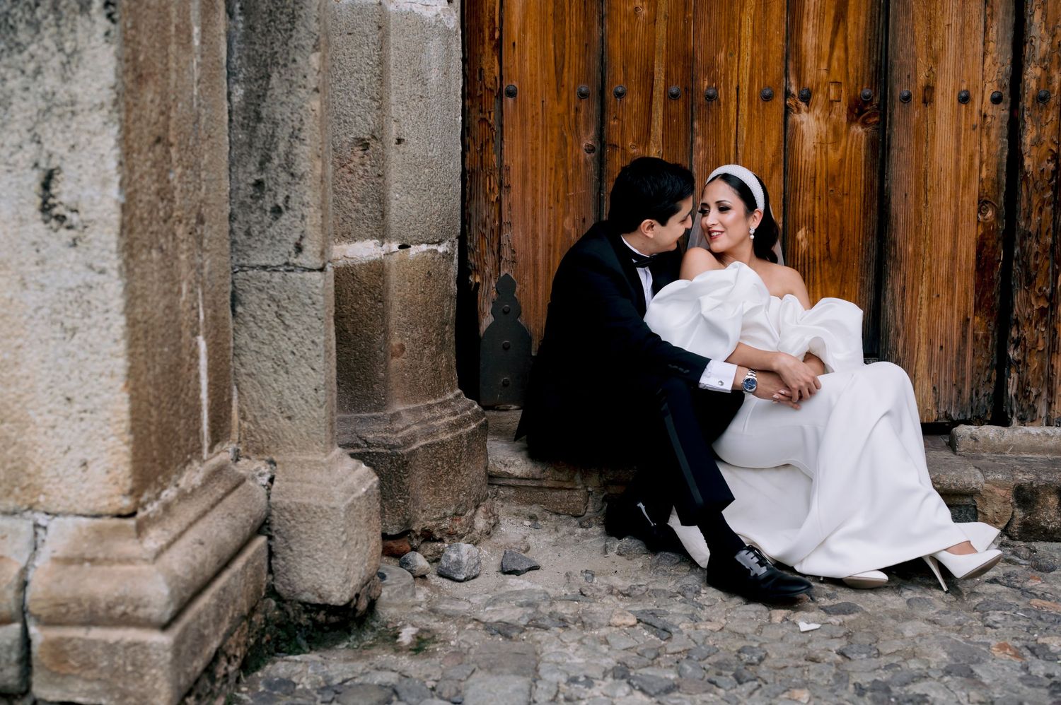 Romantic wedding couple shares intimate moment on stone steps by wooden door.