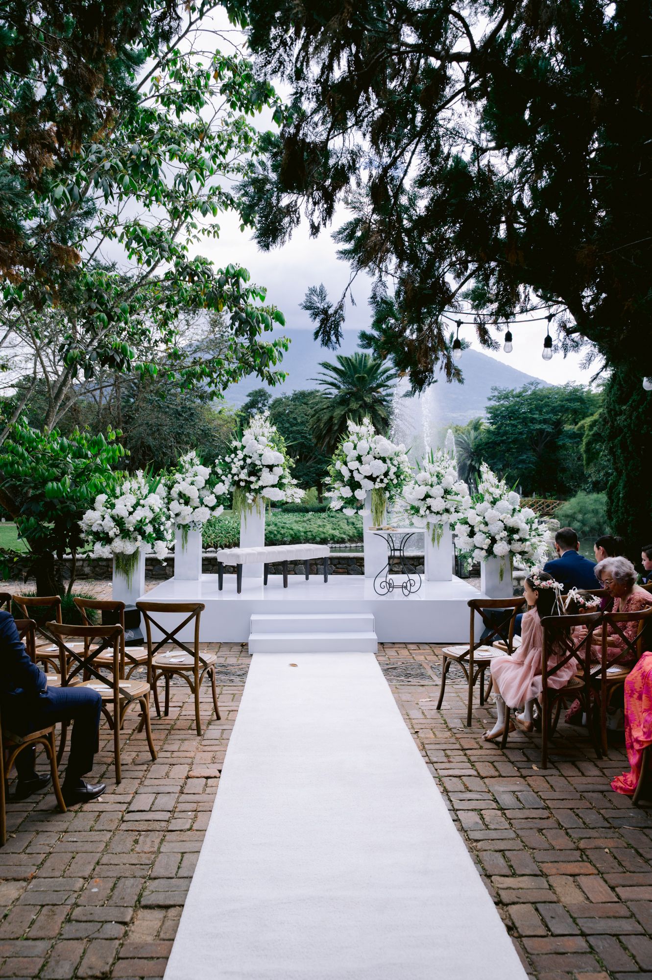Outdoor wedding ceremony setup with white aisle runner and floral arrangements on pedestals against a mountain backdrop.