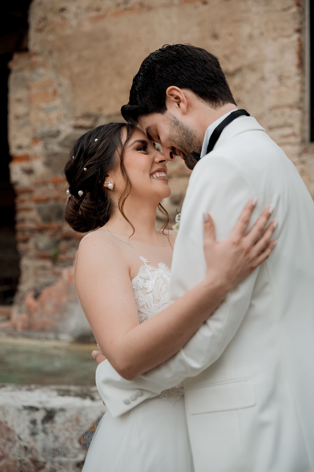 Intimate close-up of newlyweds sharing tender moment against textured stone backdrop.