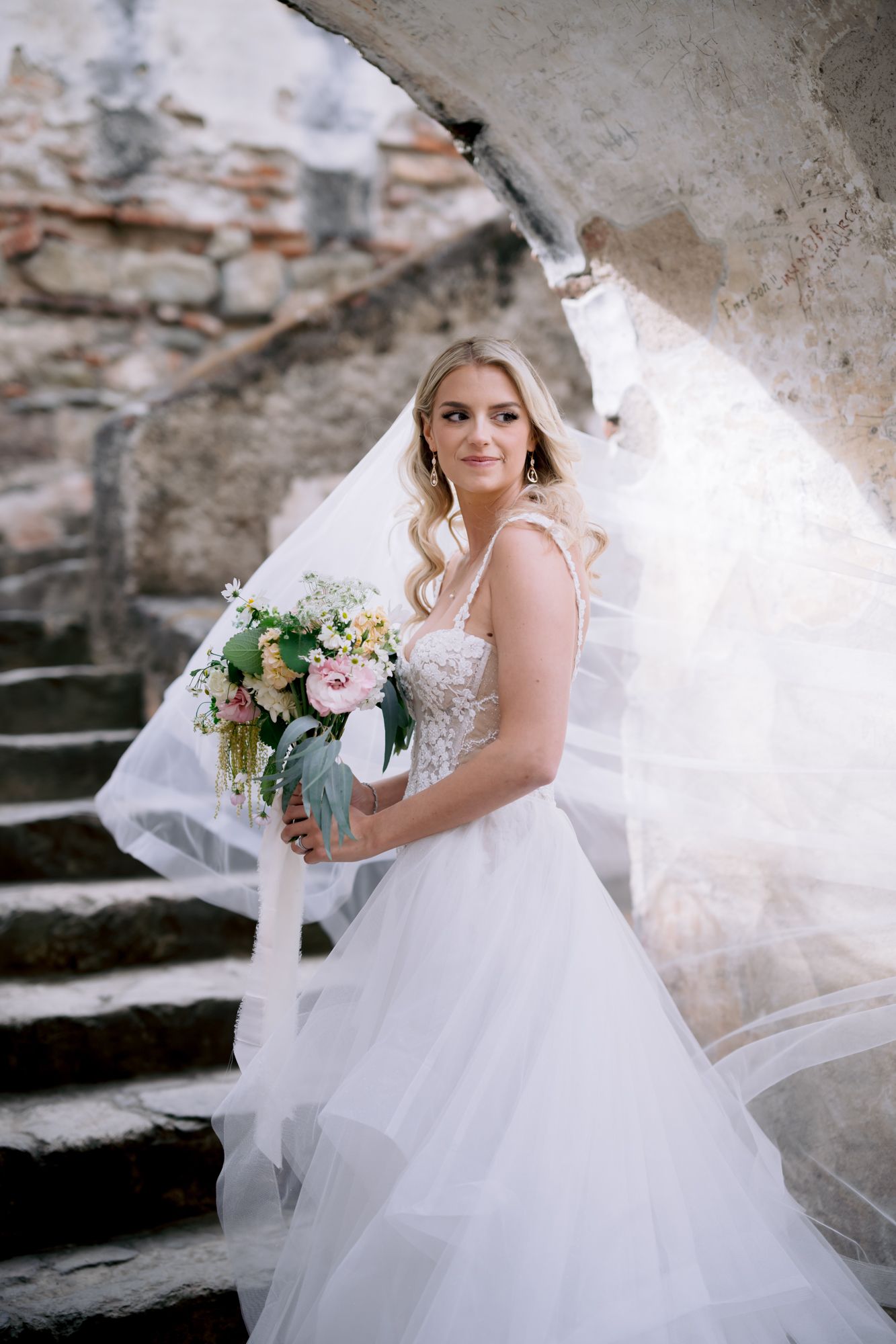 Romantic bridal portrait on stone steps with flowing tulle gown and pastel bouquet.