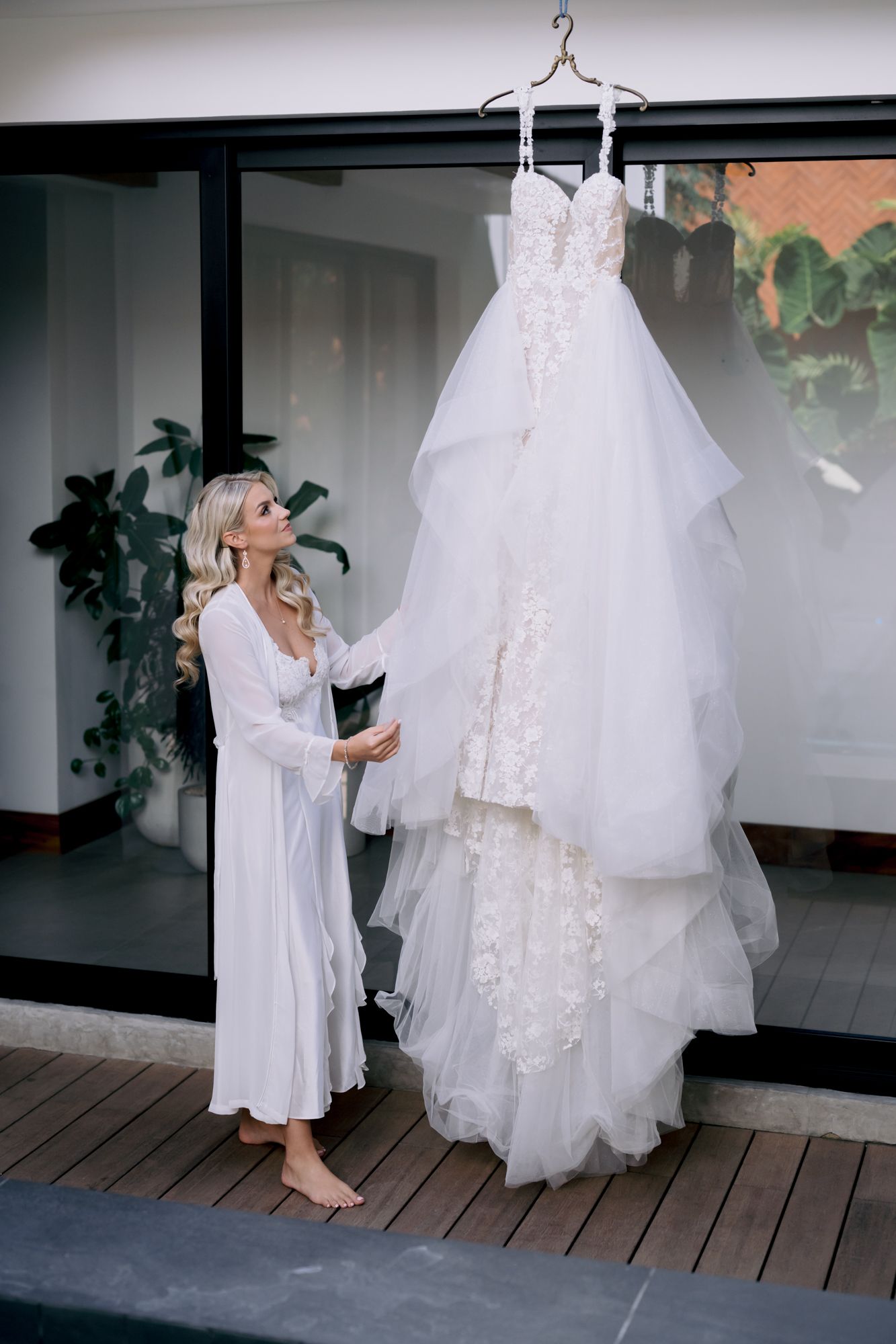 A beautiful white wedding gown with lace details hanging while someone admires it.