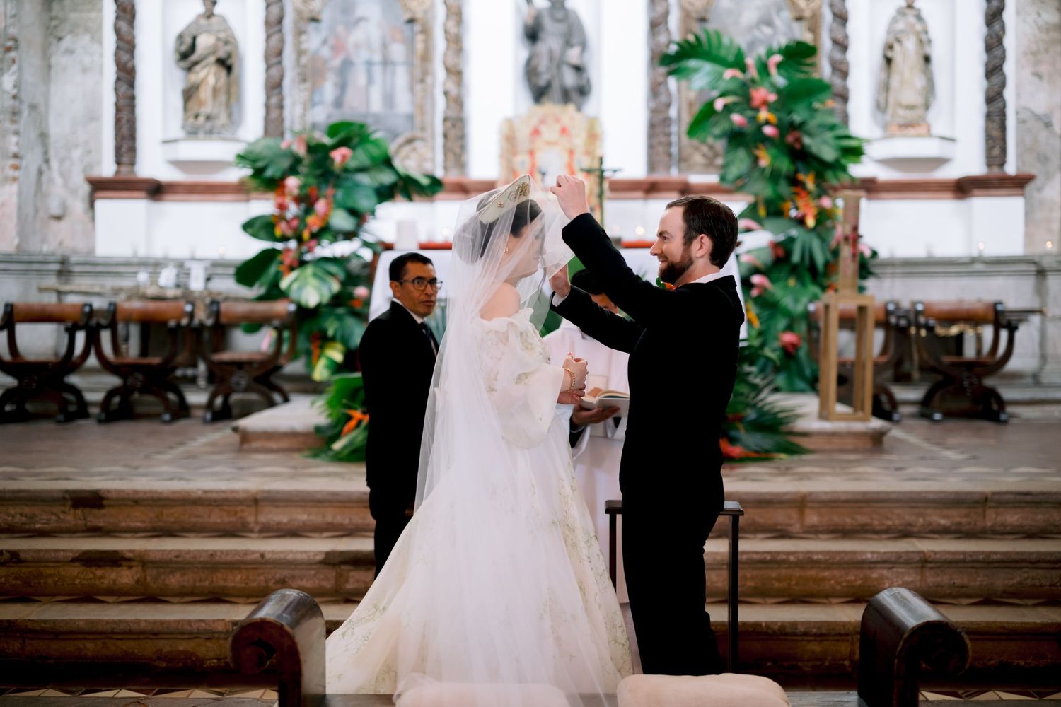 Wedding ceremony moment with the bride's veil being adjusted at the ornate church altar.