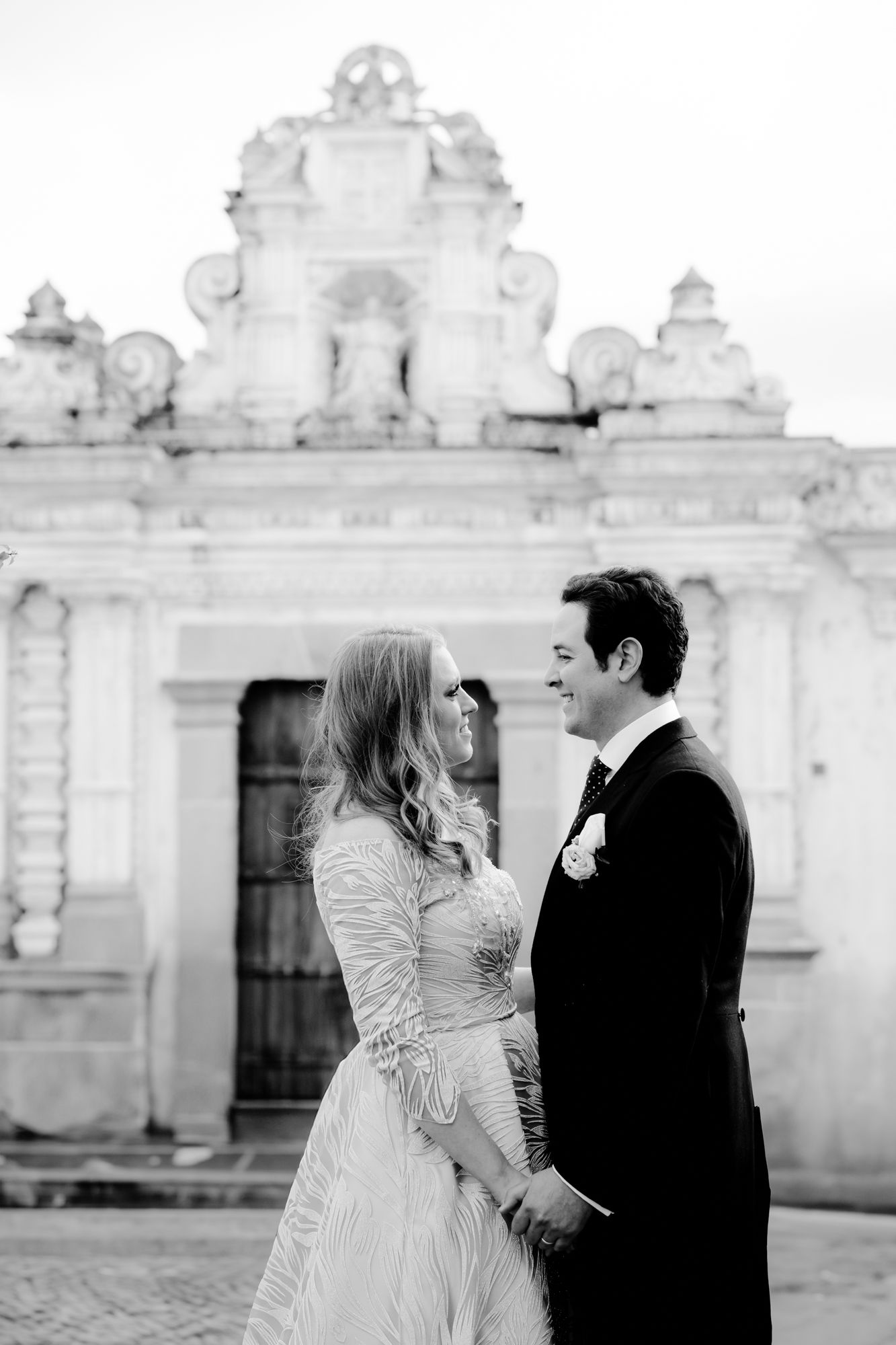 Black and white portrait of couple in front of ornate white colonial architecture.