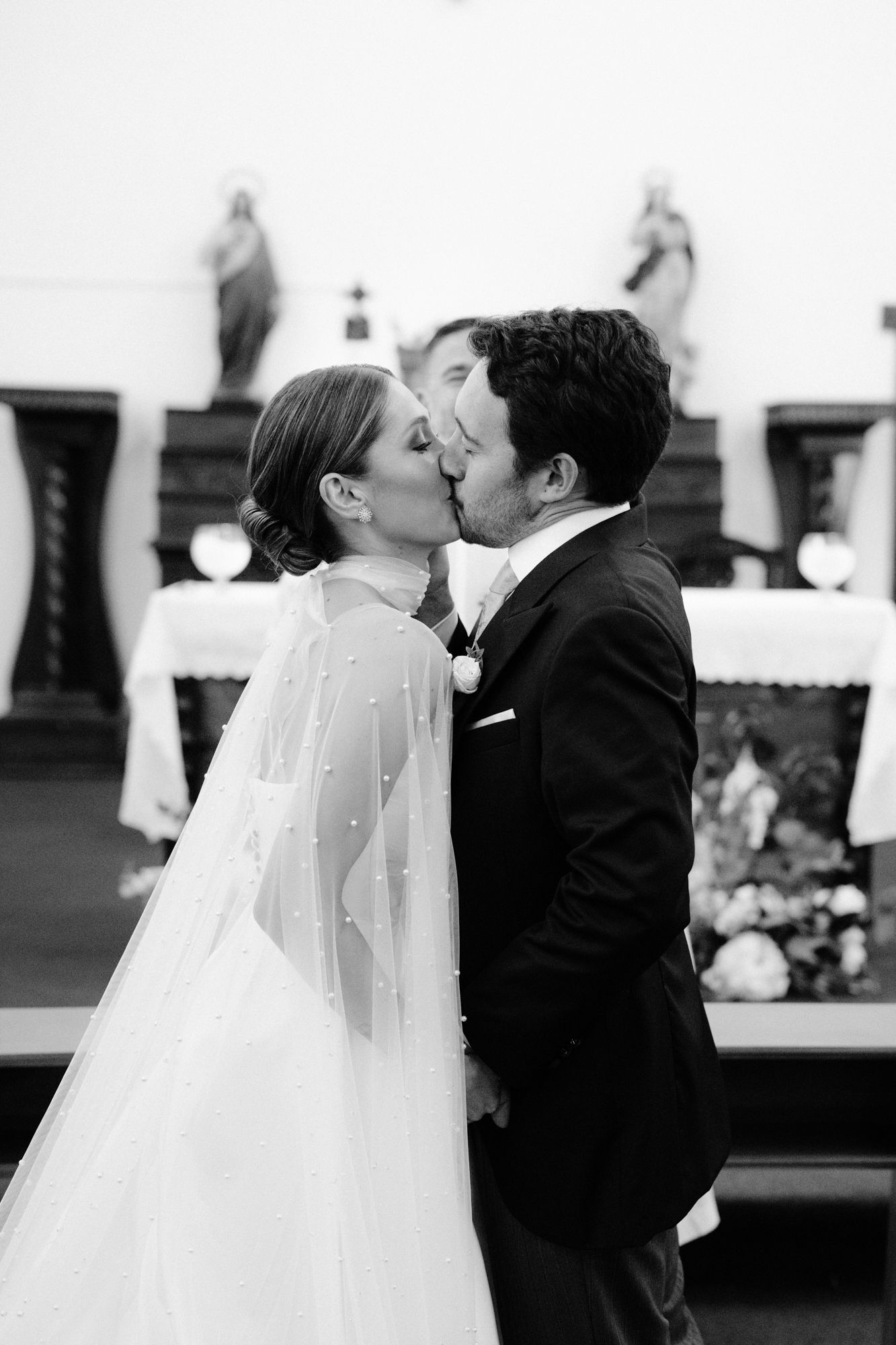 Intimate black and white photo of newlyweds sharing their first kiss during wedding ceremony.